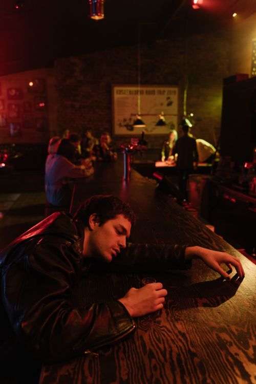 Free A man in a leather jacket appears sleepy at a dimly lit bar counter, late night vibe. Stock Photo