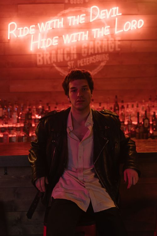 Free Man in a black leather jacket sitting at a neon-lit bar, exuding a moody vibe. Stock Photo