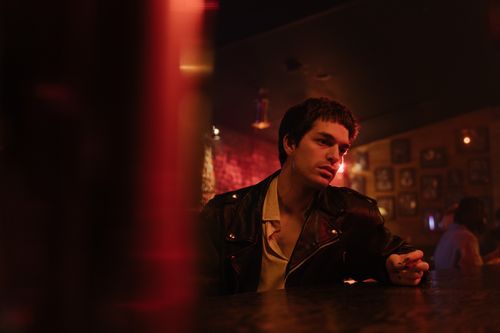 Free A young man in a leather jacket sits thoughtfully at a bar counter in dim lighting. Stock Photo