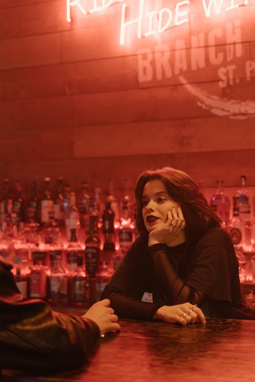 Free A young woman engaged in conversation at a stylish neon-lit bar setting. Stock Photo