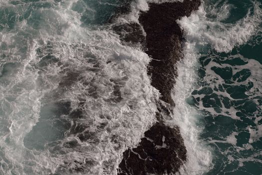 Dynamic aerial shot of waves crashing against a rocky islet.