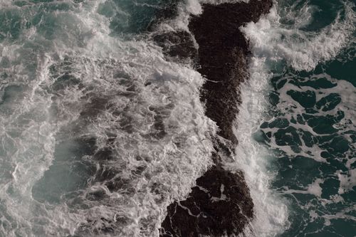 Free Dynamic aerial shot of waves crashing against a rocky islet. Stock Photo