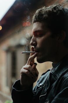 A man in a leather jacket smokes a cigarette outdoors, highlighting a moody urban lifestyle.