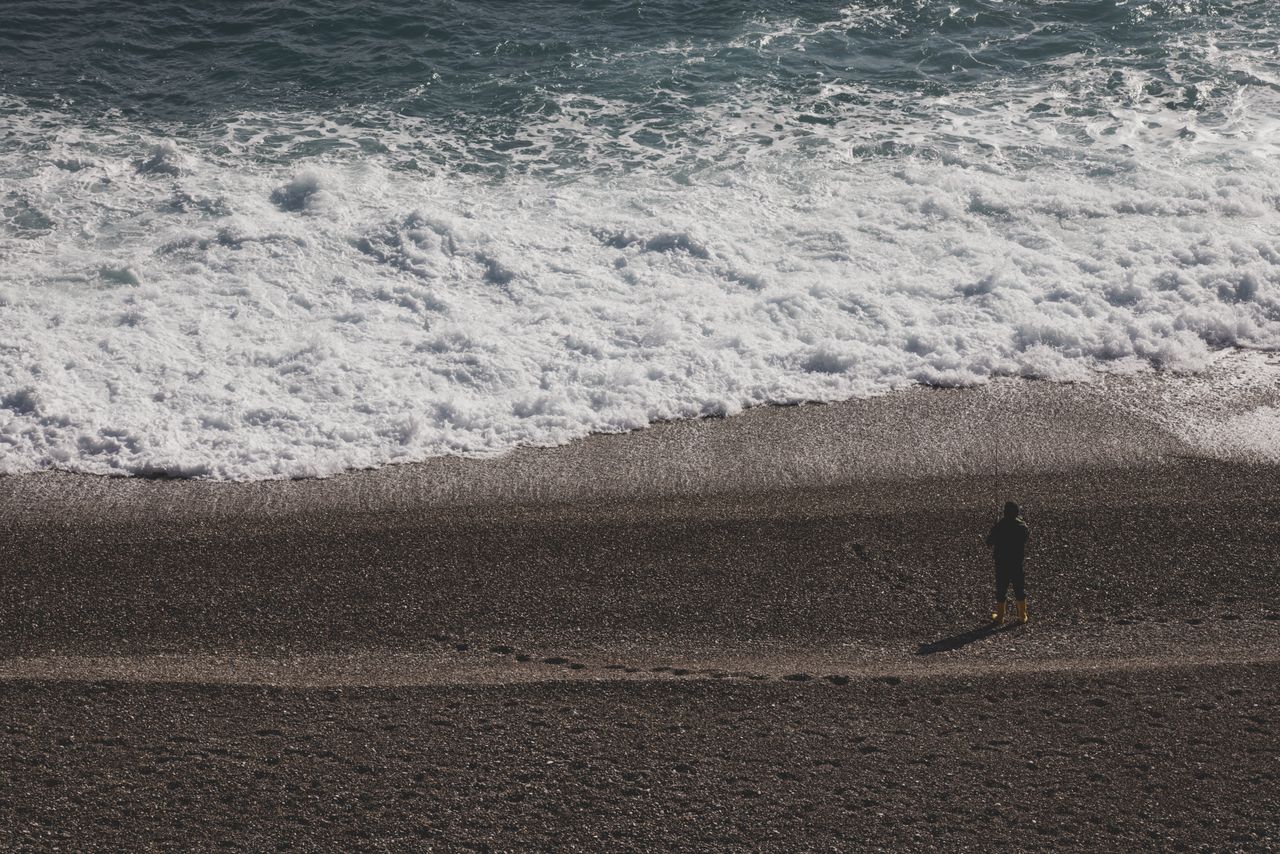 a person stands alone on a rocky beach watching the waves crash onto t