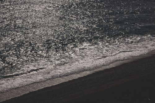 Free Aerial view of a shimmering sea shore with waves lapping onto the sandy beach in grayscale. Stock Photo