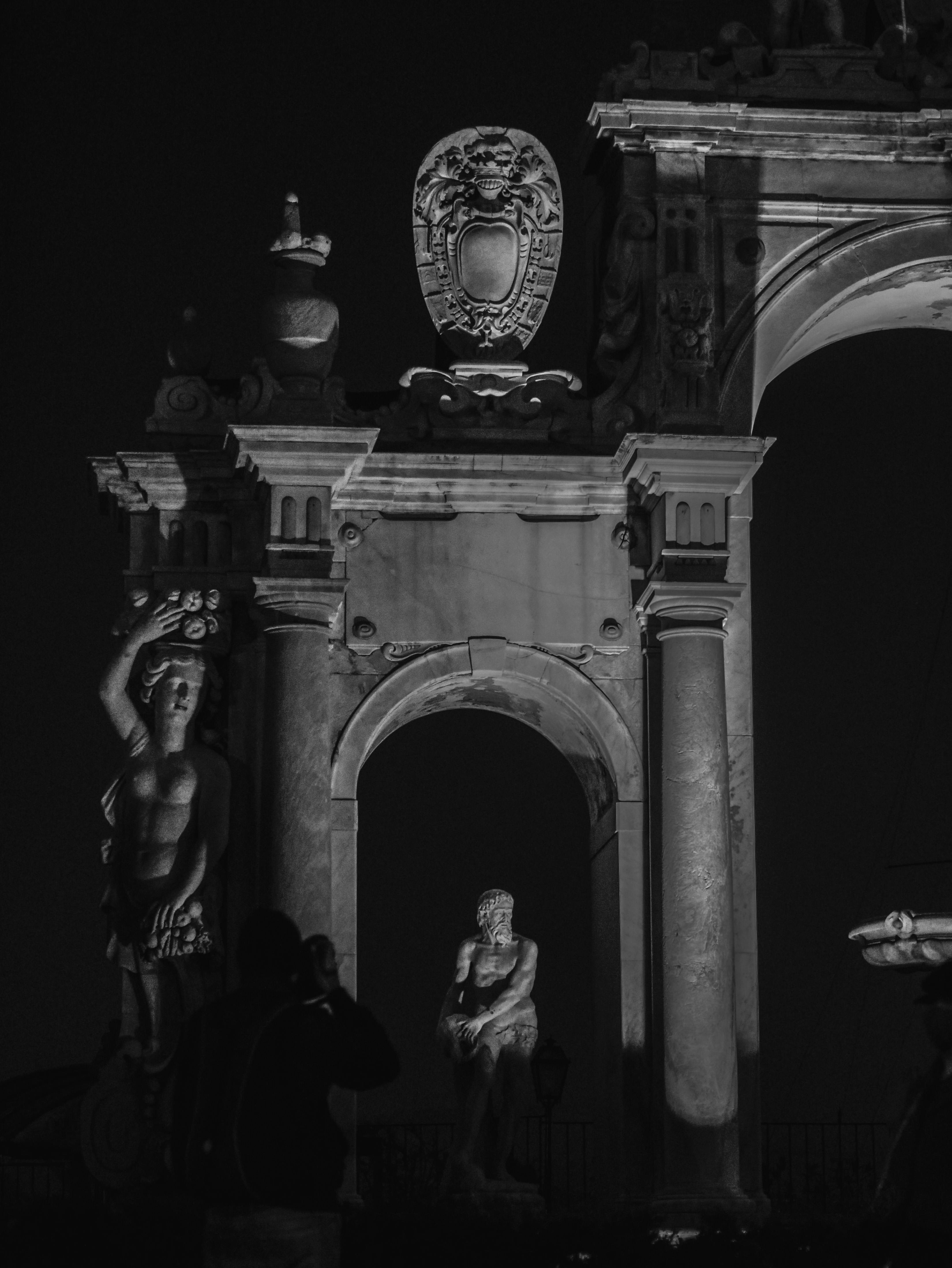 Free Dramatic night view of classical sculpture and arches in Naples, Italy, captured in black and white. Stock Photo