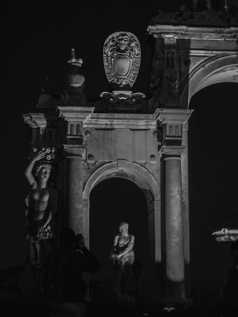 Dramatic night view of classical sculpture and arches in Naples, Italy, captured in black and white.