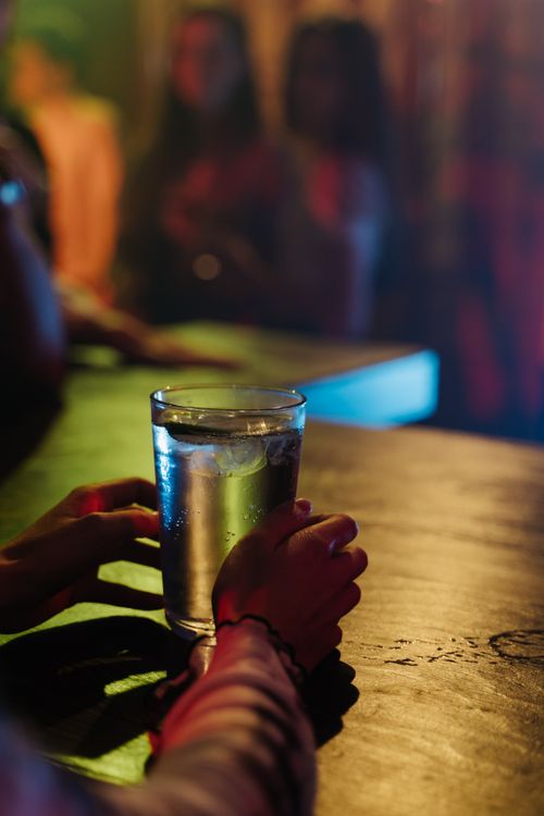 Free Close-up of a hand holding a glass on a vibrant bar counter at night. Stock Photo