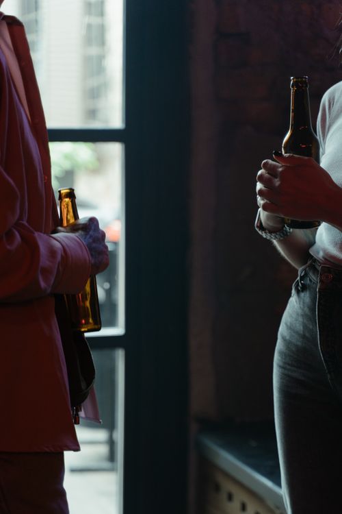 Free A scene of two people holding beer bottles and talking in a dimly lit bar. Stock Photo