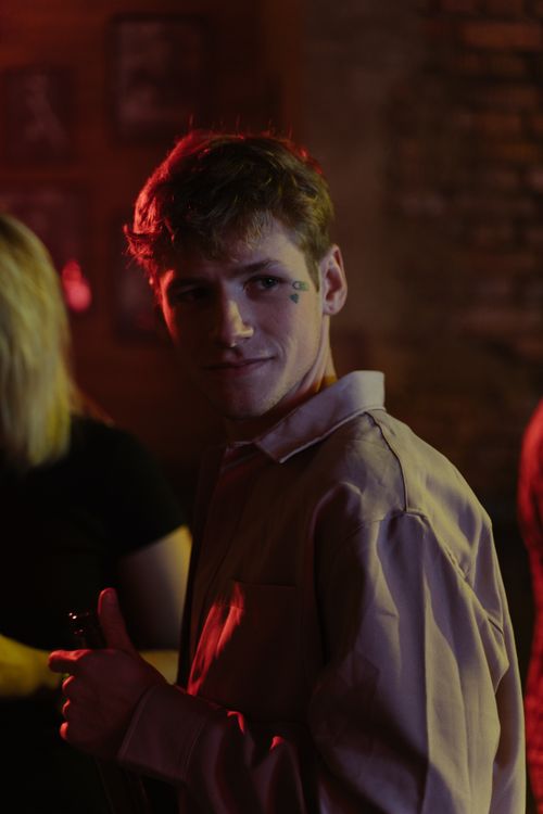 Free A young man with facial tattoos stands in a dimly lit bar, creating a moody nightlife atmosphere. Stock Photo