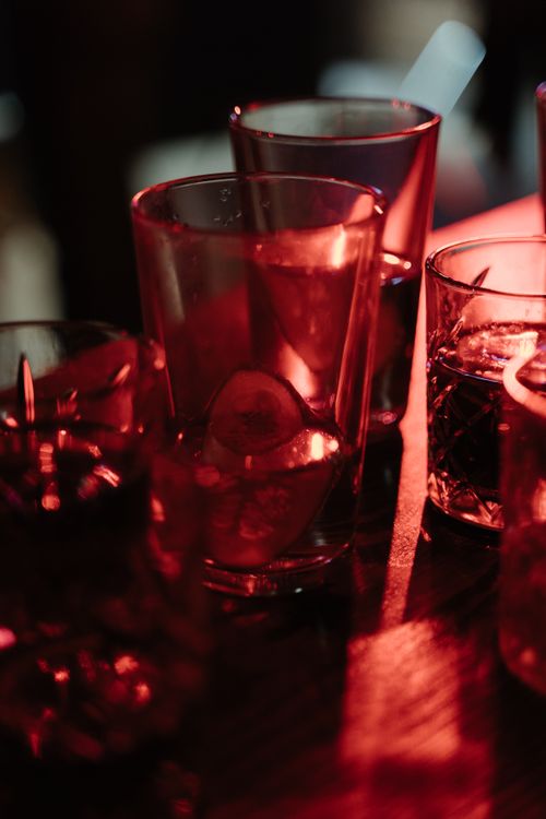 Free Close-up of cocktail glasses on a bar counter lit with warm red lighting. Stock Photo