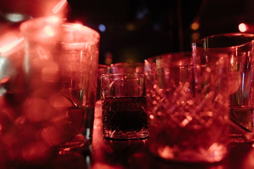 A collection of illuminated glasses on a bar with dramatic red lighting, creating a moody ambiance.