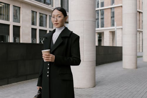 Free A Woman in Black Coat Wearing Eyeglasses while Holding a Cup of Coffee Stock Photo