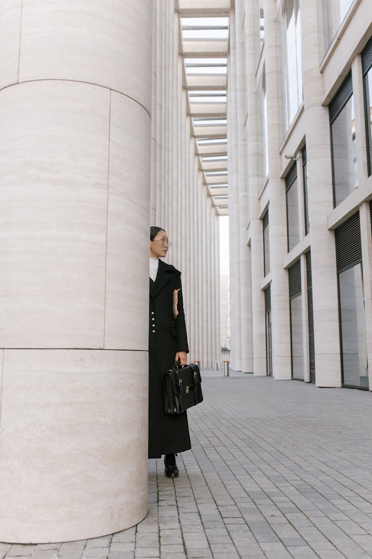 A Woman In Black Coat Standing While Holding Her Briefcase