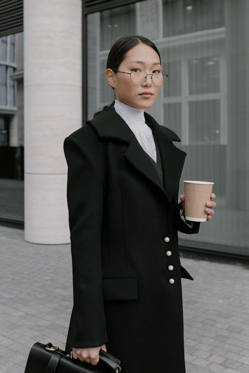 Free A Woman in Black Coat Wearing Eyeglasses while Holding a Cup of Coffee Stock Photo