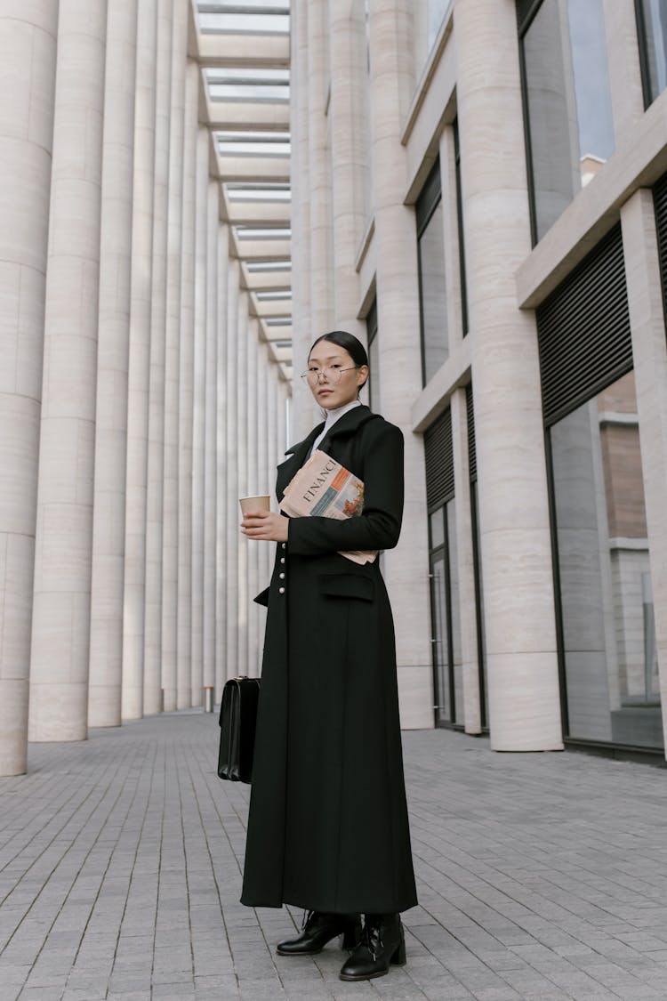 Woman In Black Coat Holding Newspaper And Coffee To Go