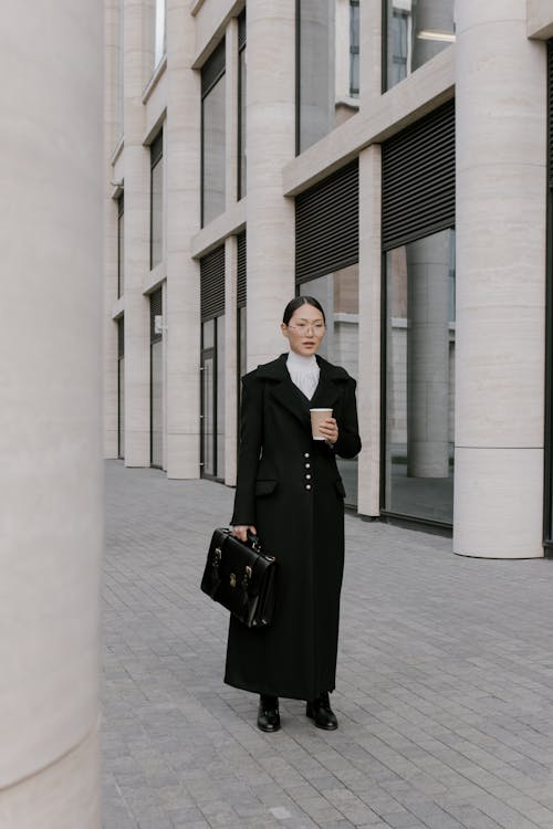 Woman in Black Coat Holding Newspaper and Coffee to Go · Free Stock Photo