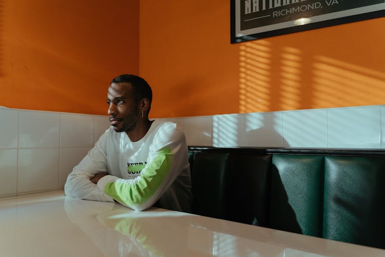 A Man In White Long Sleeves Sitting On The Couch Of A Cafe While Looking Afar