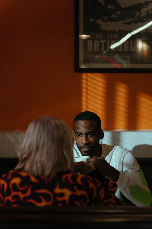 A Man in White Sweater Sitting in Front of a Woman Wearing Printed Jacket Holding a Cup