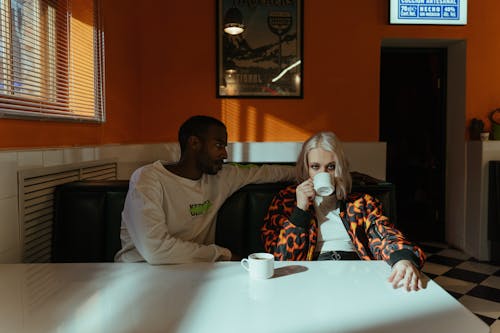 A Man in White Sweater Looking at the Woman Drinking on a Mug