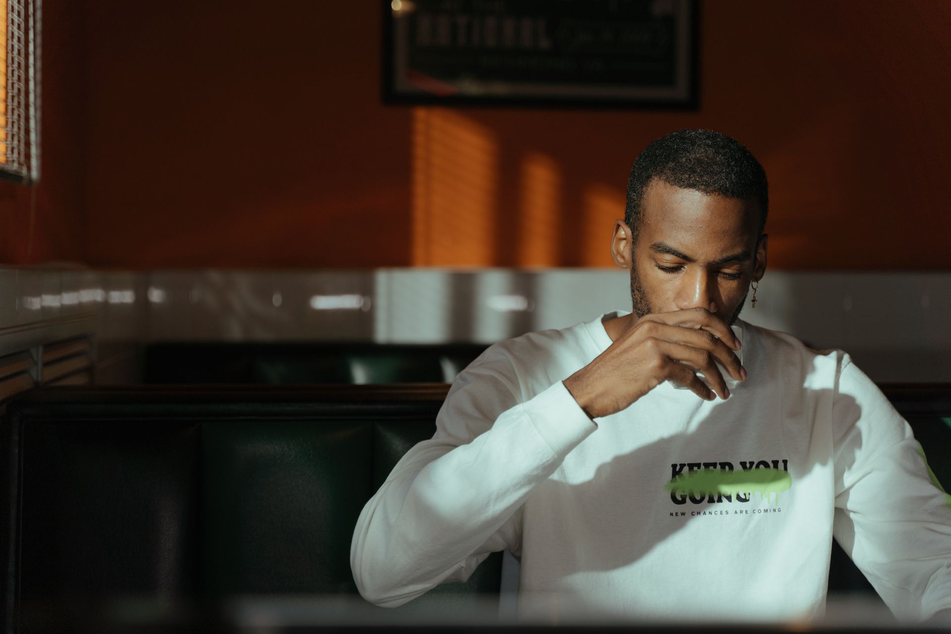 A young man in white long sleeves enjoys a quiet moment in a cafe, sipping a beverage.