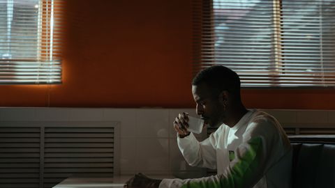 A man seated in a café, enjoying a cup of coffee with sunlight streaming through the windows.