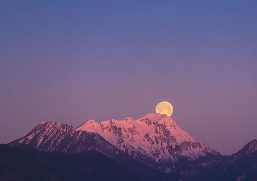 Free Supermoon setting behind snow-covered mountains in Lower Austria at twilight. Captivating winter landscape. Stock Photo