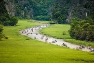 Crowd of people floating on river between grassy fields near green lush trees during trip in Vietnam in Tam Coc
