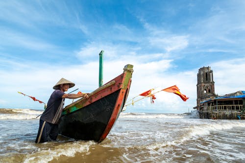 Asian man in Vietnamese hat standing near boat in water