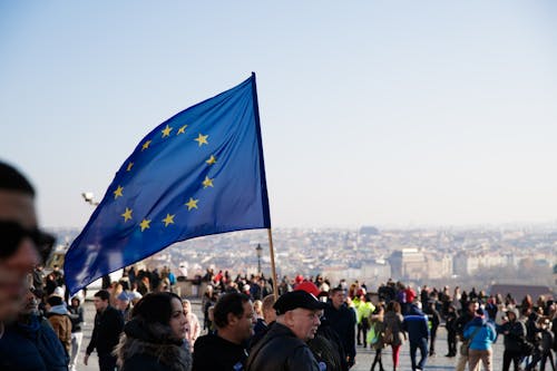 Crowd of people walking on street with waving flag of European Union Courtesy during protest in city against residential buildings