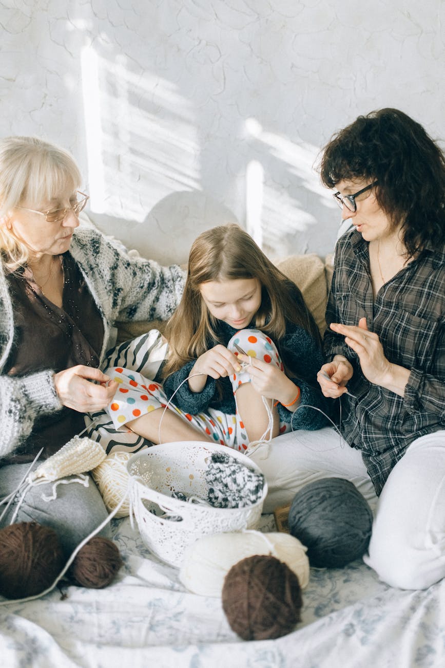 Grandmother, mother, and girl knitting together in a cozy setting.