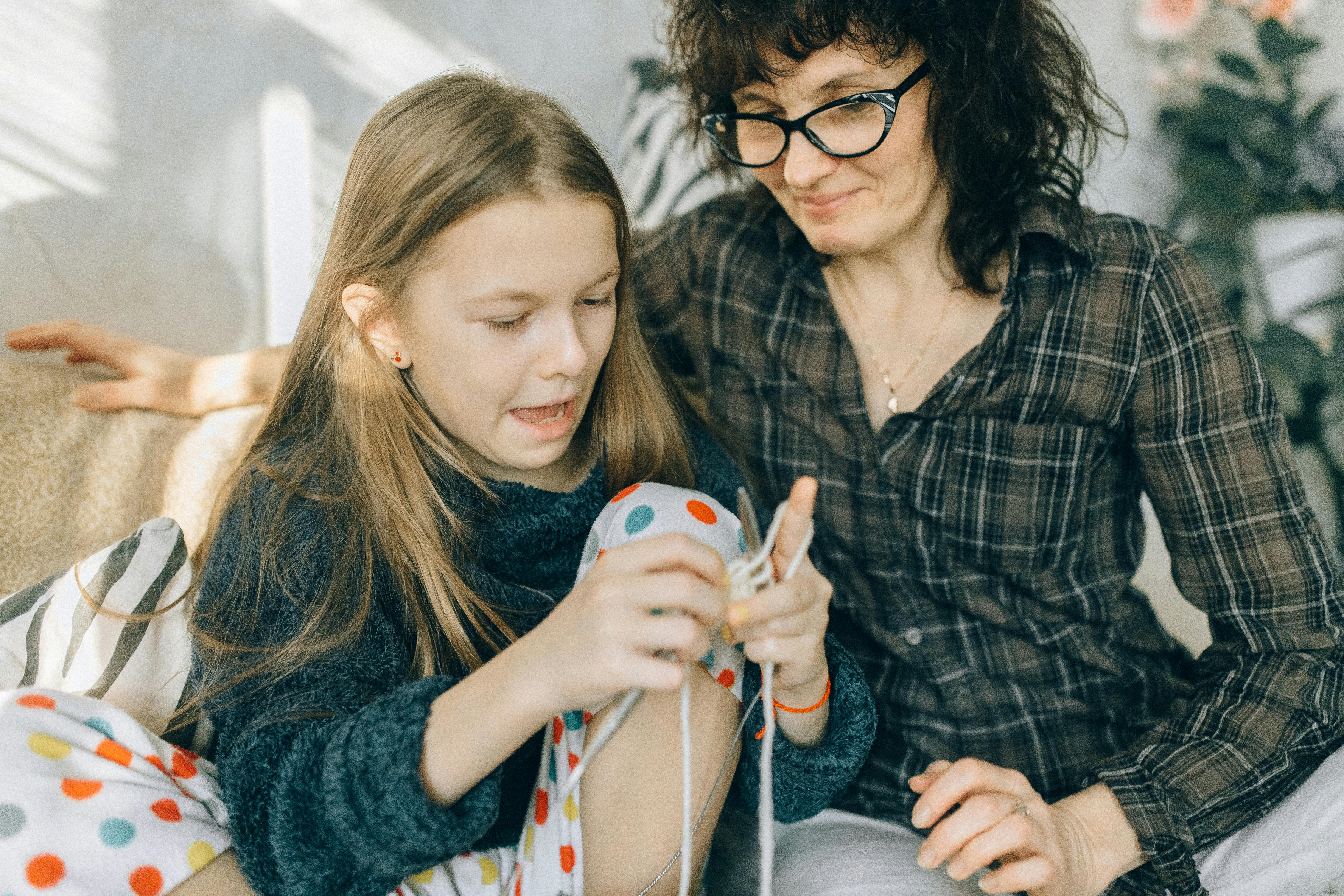 A mother and daughter sharing quality time while crocheting together indoors.
