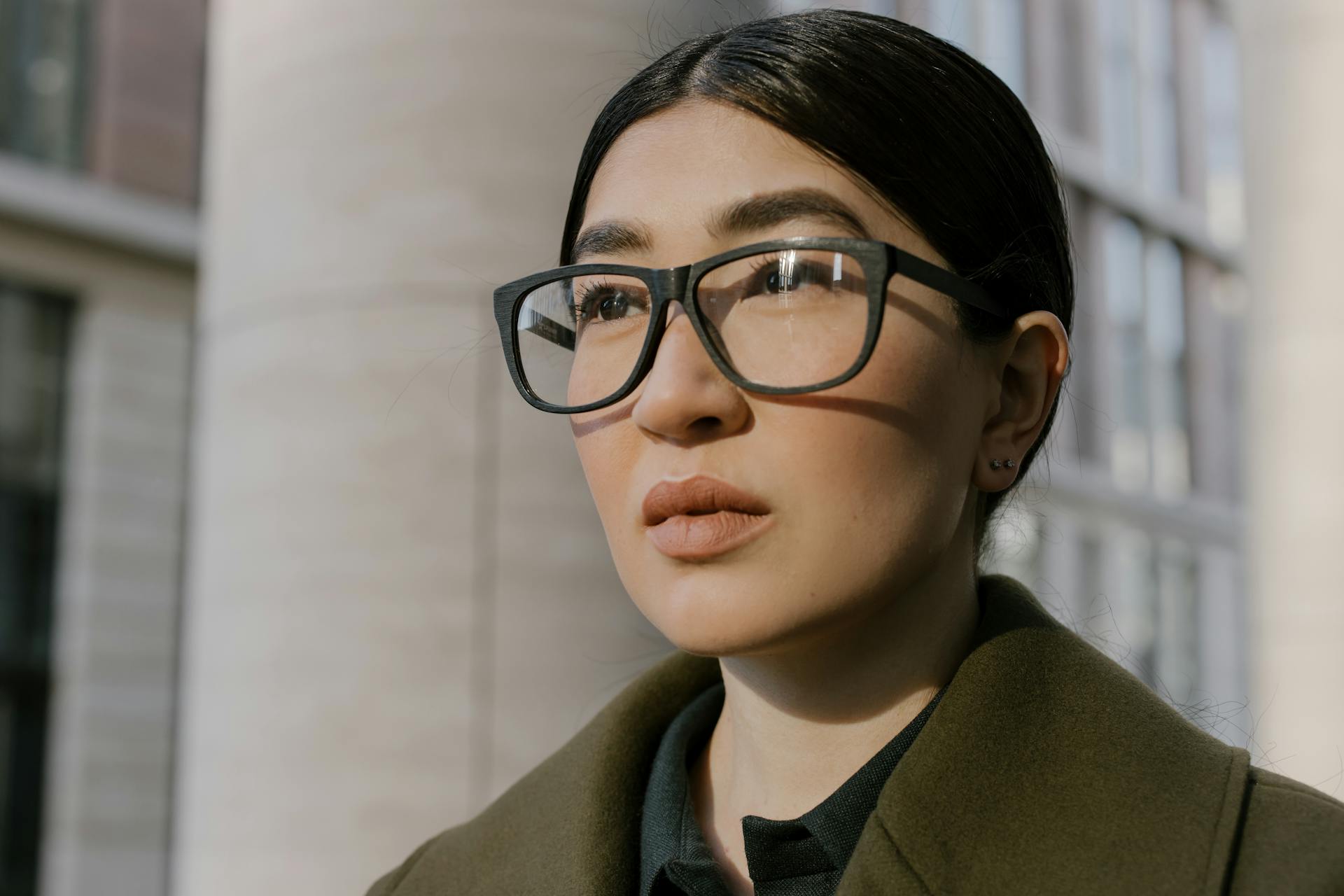 Close-up portrait of a confident woman in glasses, exuding professionalism in an urban environment.