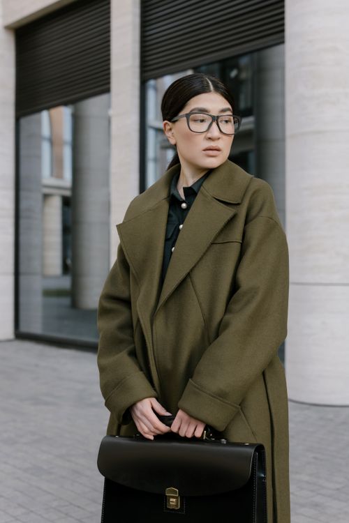 Free Elegant woman in a green coat holding a briefcase, standing outside modern building. Stock Photo