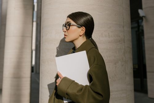 Free Side view of a professional woman holding documents outdoors, showcasing a modern business look. Stock Photo