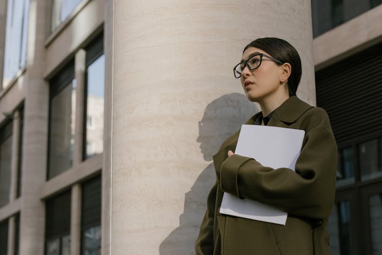 Woman In Black Framed Eyeglasses And Green Coat Near The Wall