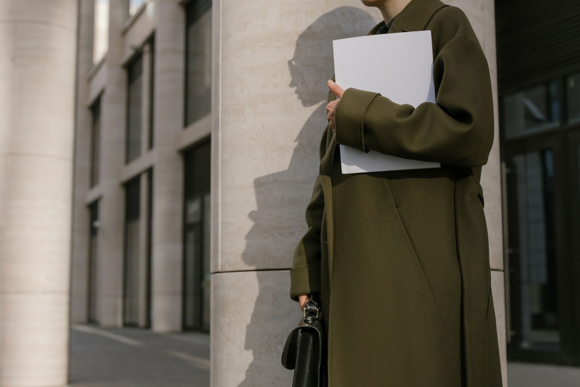 Woman in a green coat holding documents outside a modern office building.