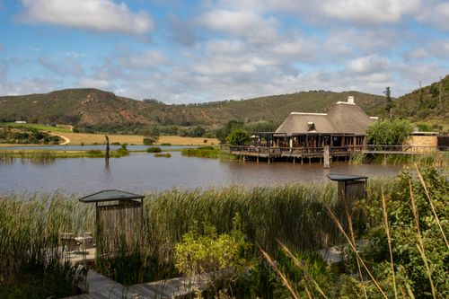 Free Charming countryside lodge with thatched roof by a peaceful lake surrounded by lush hills. Stock Photo