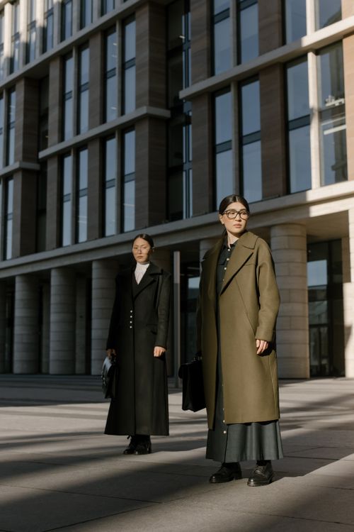 Free Two fashionable Asian women in coats, standing confidently outside a modern office building. Stock Photo