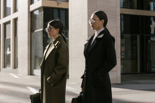 Free Two stylish women standing outside an urban office building, dressed in formal coats. Stock Photo