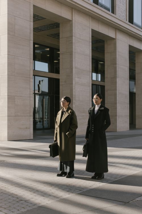 Free Two young professionals in stylish coats stand confidently outdoors, showcasing modern work fashion. Stock Photo