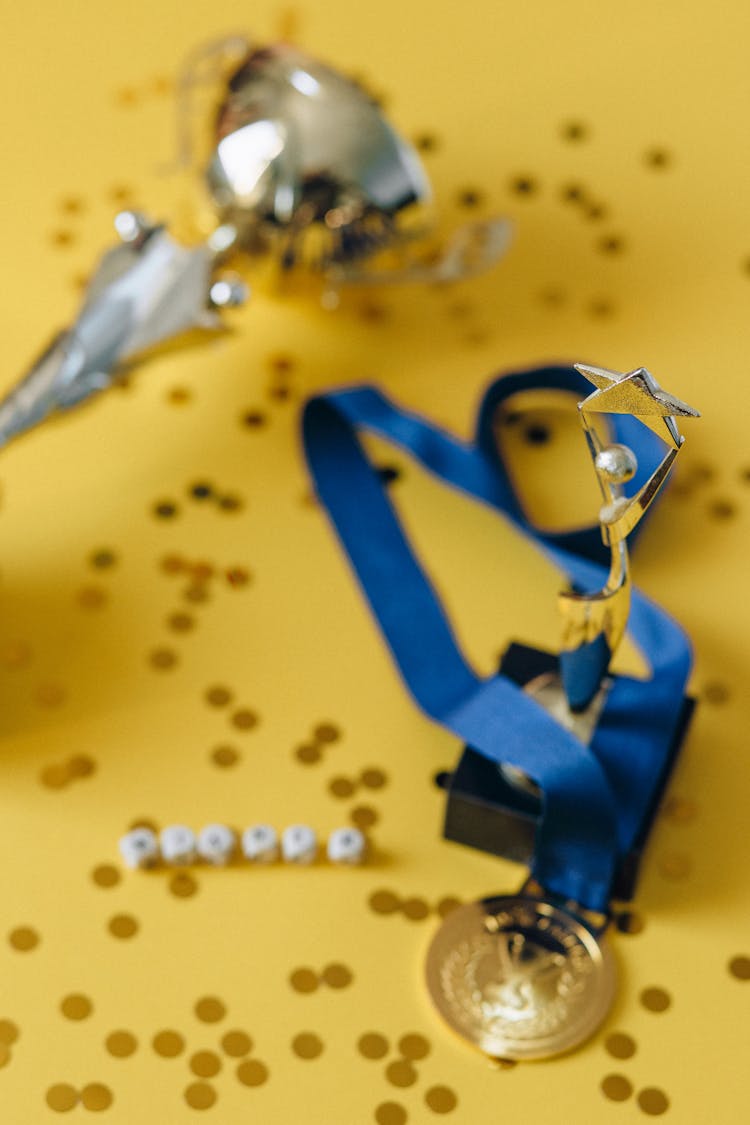 Medal On Blue Ribbon Beside Golden Statuette On Yellow Background