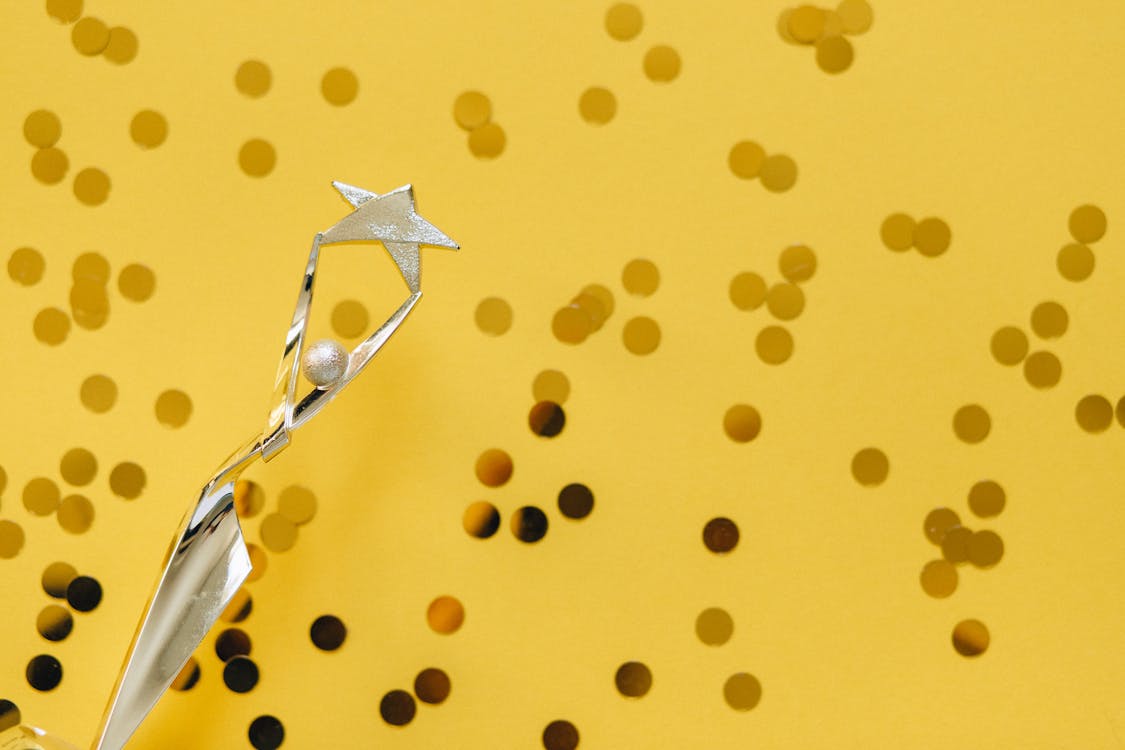 Free A silver trophy with a star design on a vibrant yellow background adorned with confetti. Stock Photo