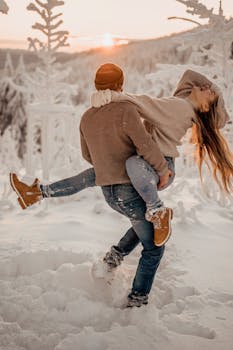 A couple enjoys a playful moment in a scenic snowy landscape during sunset.
