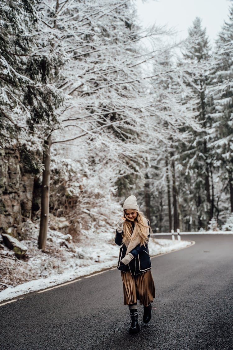 Woman In Winer Coat And Brown Skirt Walking On The Road In Snowy Forest