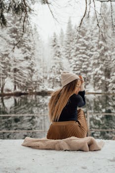 A woman sits by a tranquil snow-covered lake in Munich, Germany, embracing the winter chill.