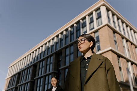 Two stylish women in coats in a business district with modern architecture.