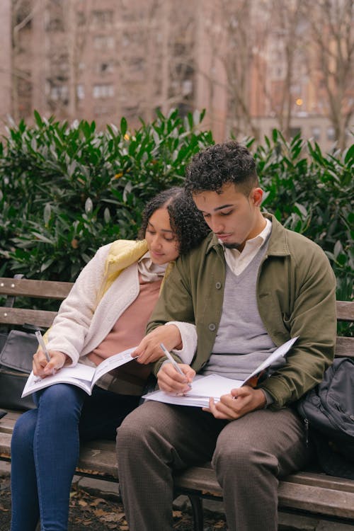 Free Focused couple writing in workbooks on bench in park Stock Photo