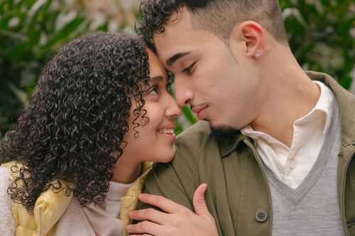 Free Happy ethnic crop couple hugging and looking to each other while spending time together in park and smiling at daytime Stock Photo