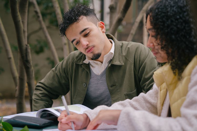 Hispanic Couple Studying On Street At Table With Books